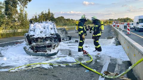 Ausgebranntes Auto auf Autobahn, daneben Feuerwehrkräfte