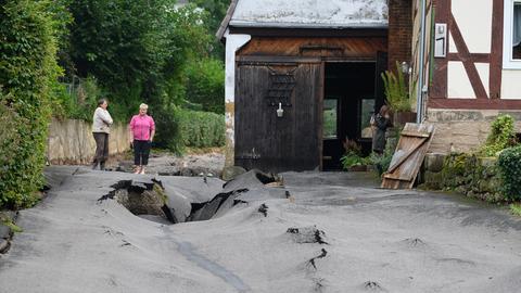 Die Anwohnerinnen Christina Wiesmann-Günter (l) und Silke Kompfe stehen nach einem Unwetter in dem Trendelburger Stadtteil Gottsbüren an einer zerstörten Fahrbahndecke.