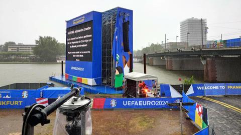 Das Bild zeigt die leere Fanmeile Frankfurt am Mainufer. Auf einem Bildschirm ist zu lesen, dass die Besucherinnen und Besucher den Bereich verlassen sollen.