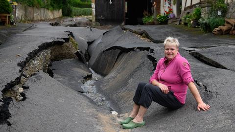 Anwohnerin Silke Kompfe hockt nach einem Unwetter in dem Trendelburger Stadtteil Gottsbüren an einer zerstörten Fahrbahndecke.