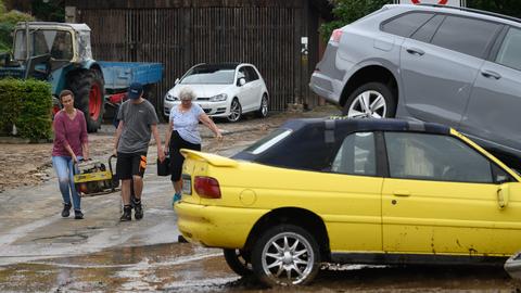 Helfer gehen an zwei zerstörten Autos nach einem Unwetter in dem Trendelburger Stadtteil Gottsbüren vorbei.