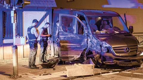 Ein zerstörter Transporter steht an einer Straßenecke, daneben Polizisten.