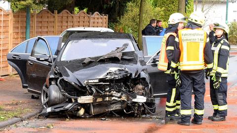 Einsatzkräfte stehen um einen schwarzen Mercedes AMG mit völlig zerstörter Motorhaube herum.