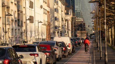 Viele Autos, daneben Radfahrer auf Radweg, im Hintergrund Hochhäuser