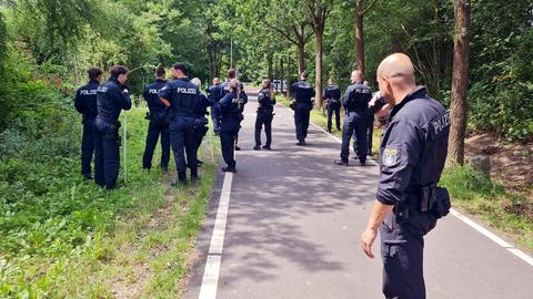 14 Polizeikräfte stehen auf einem Radweg, der von Gebüsch umgeben ist.