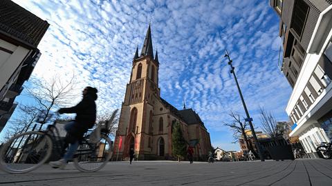 Platz mit einer Kirche, eine Radfahrerin ist verschwommen im Vordergrund zu erkennen.