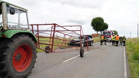 An der Front beschädigtes Auto hinter Traktor mit leerem Viehgitter