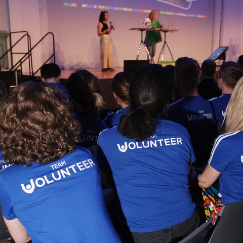 Menschen in einem Saal von hinten fotografiert - T-Shirt-Aufschrift Team Volunteer