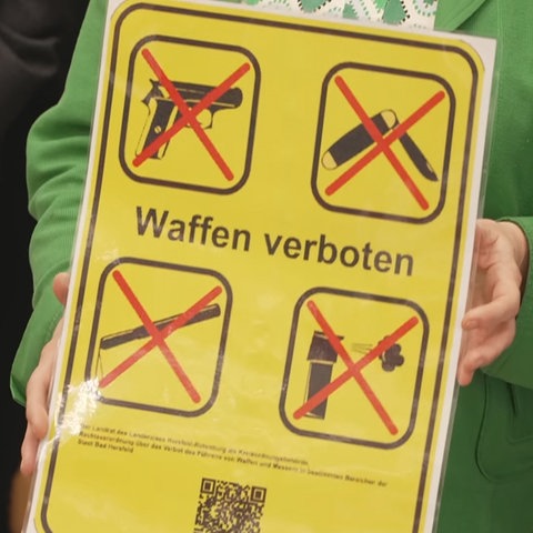 "Waffen verboten" steht auf einem Schild. Abgebildet sind eine Pistole, ein Messer und weitere Gegenstände.