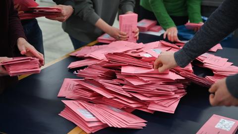 Wahlhelfer und Wahlhelferinnen sortieren Briefwahlumschläge.