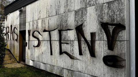 An einem Haus mit weißer Steinmauer ist in schwarz "RASSISTEN!" gesprüht