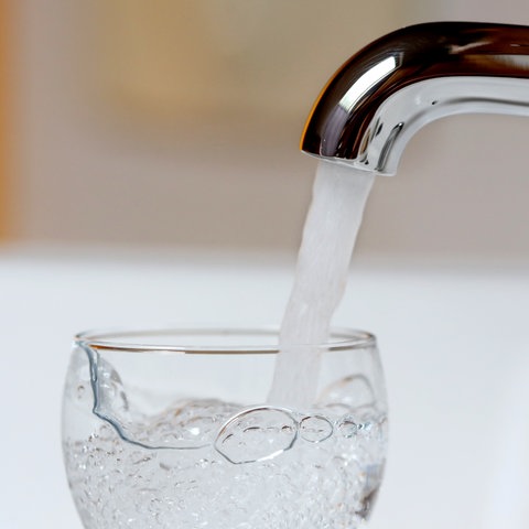 Wasser läuft aus einem Wasserhahn in ein Glas.