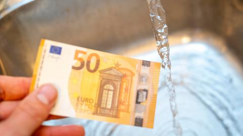 Eine Hand mit einem 50-Euro-Schein unter einem laufenden Wasserhahn