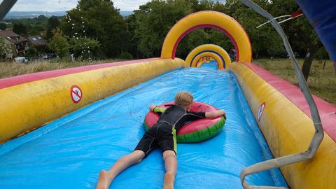 Ein Junge rutscht mit einem Reifen die bunte, aufblasbare Wasserrutsche runter