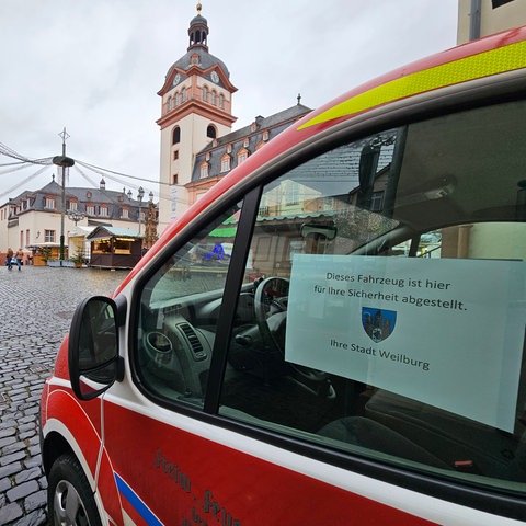 Ein Fahrzeug der Feuerwehr steht auf einem Zugangsweg zum Weihnachtsmarkt in Weilburg. In der Fensterscheibe eine Notiz: Dieses Fahrzeug ist hier für ihre Sicherheit abgestellt. Ihre Stadt Weilburg