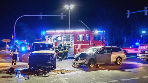 Zwei zerstörte Autos bei Dunkelheit auf einer Kreuzung vor einem Feuerwehrwagen, außerdem mehrere einsatzkräfte