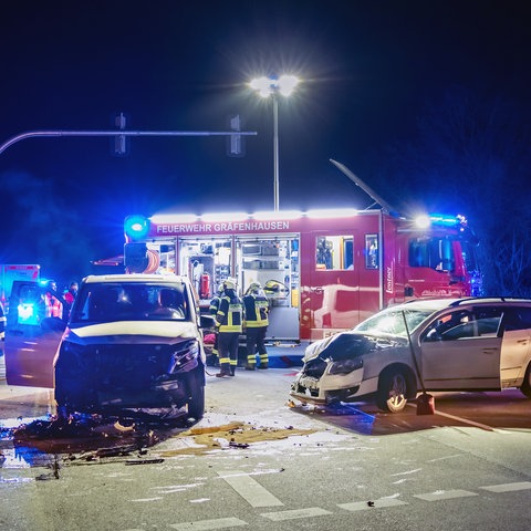 Zwei zerstörte Autos bei Dunkelheit auf einer Kreuzung vor einem Feuerwehrwagen, außerdem mehrere einsatzkräfte