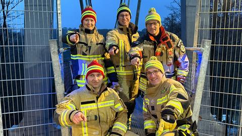 Vier Feuerwehrmänner und eine Feuerwehrfrau stehen bzw. knieen vor der Hängebrücke. Sie schauen lachend in die Kamera.