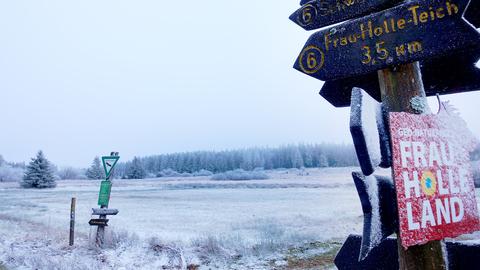 Schneebedecktes Feld. Im Vordergrund eingeschneite Schilder mit der Aufschrift "Frau Holle Land" und "Frau Holle Teich"