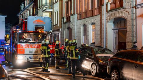 Feuerwehrleute stehen vor einem Altbau. Daneben liegen dicke Wasserschläuche. 