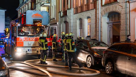 Feuerwehrleute stehen vor einem Altbau. Daneben liegen dicke Wasserschläuche. 