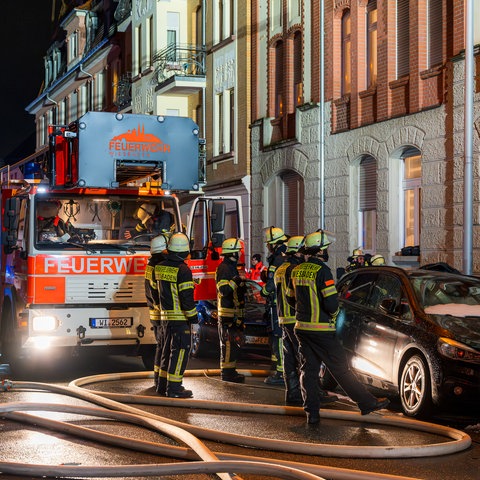 Feuerwehrleute stehen vor einem Altbau. Daneben liegen dicke Wasserschläuche. 