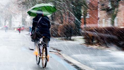 Fahrradfahrer bei Schneeregen mit Schirm in der Hand