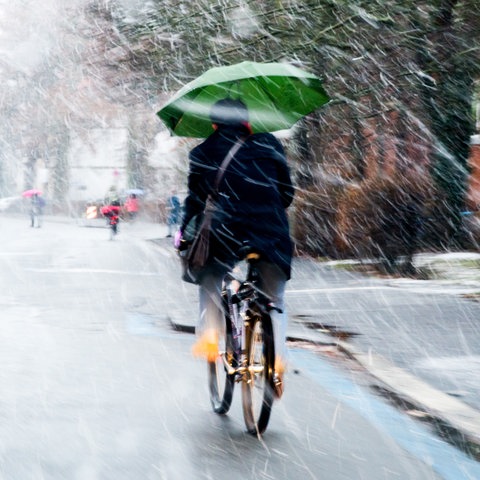 Fahrradfahrer bei Schneeregen mit Schirm in der Hand