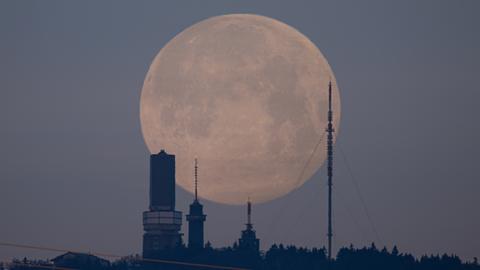 Gebäude auf dem Feldberg sind als Silhuette vor dem Vollmond zu erkennen, der wie ein riesiger Ballon erscheint.