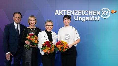 Die Frauen Maika Janat-Vennemann, Emma Hufnagel und Elvira Bunzel halten Blumensträuße in den Händen. Sie stehen neben dem Mann Rudi Cerne, dem Moderator der Fernsehsendung Aktenzeichen XY ungelöst.