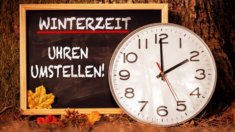 Uhr auf "2 Uhr", daneben Tafel mit der Aufschrift: "Winterzeit - Uhren umstellen"