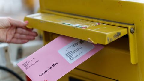 Eine Frau wirft ihre Briefwahlunterlagen zur Oberbürgermeisterwahl in Frankfurt in einen Briefkasten. 