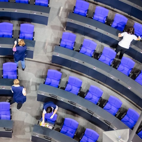 Von oben fotografierte vier Reinigungskräfte, die die Tische im Plenarsaal des Bundestags abwischen