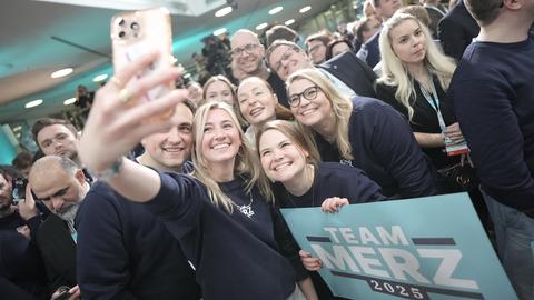 Blonde Anhängerinnen der CDU machen ein Selfie von sich und einem Plakat mit der Aufschrift "Team Merz"