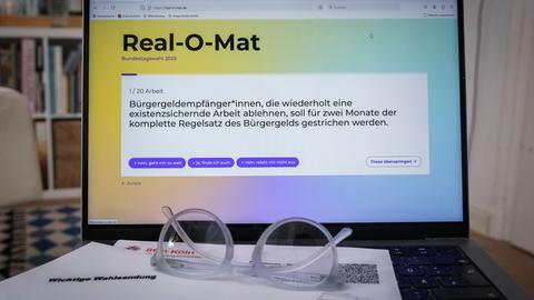 Auf einem Laptop ist die Webseite "Real-O-Mat" geöffnet. Davor liegt eine Brille auf dem Tisch.