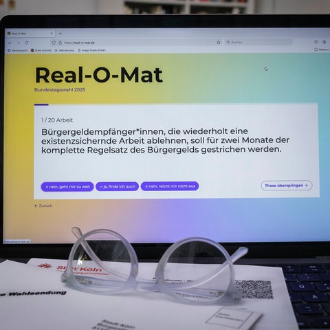 Auf einem Laptop ist die Webseite "Real-O-Mat" geöffnet. Davor liegt eine Brille auf dem Tisch.