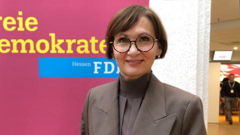 Eine Frau steht vor einer Wand und lacht in die Kamera. An der Wand steht "Freie Demokraten - Hessen FDP".