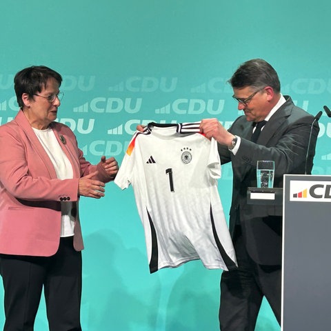 Ministerpräsident Rhein übergibt Patricia Lips ein Trikot mit der Aufschrift "1".