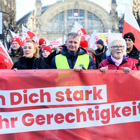 "Mach Dich stark für mehr Gerechtigkeit!" steht auf einem roten Banner, dass Demonstranten tragen; dahinter weitere Demonstranten mit DGB-Fahnen und der Frankfurter Hbf