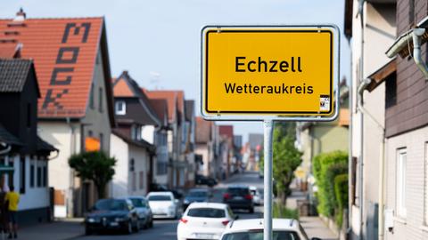 Blick in eine Straße (unscharf), in der Mitte ein gelbes Ortseingangsschild (scharf) mit der Aufschrift "Echzell" steht. 