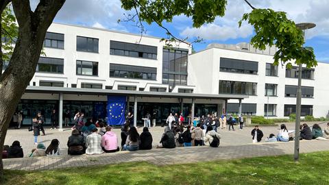 Schülerinnen und Schüler auf einem Schulhof, an der Schule hängt eine Europaflagge.