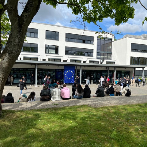Schülerinnen und Schüler auf einem Schulhof, an der Schule hängt eine Europaflagge.
