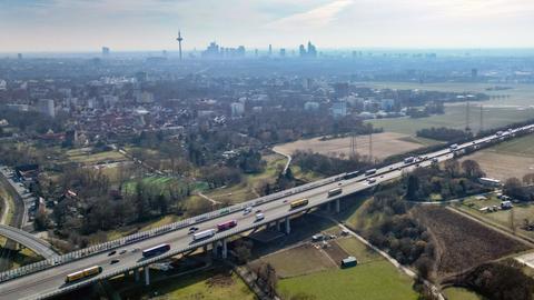 Luftaufnahme von nordwestlichen Stadtteilen von Frankfurt am Main und der A5 zwischen Westkreuz und Nordwestkreuz. Man sieht Äcker und Wiesen mit Bäumen, wo ein neuer Stadtteil gebaut werden soll. Im Hintergrund sind die Hochhäuser der Frankfurter Skyline zu sehen.