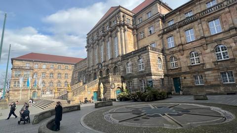 Das Rathaus in Kassel, zu sehen ist die große Treppe aus Stein, rechts und links zwei goldene Löwen. Im Vordergrund ist der Aschrottbrunnen zu sehen.