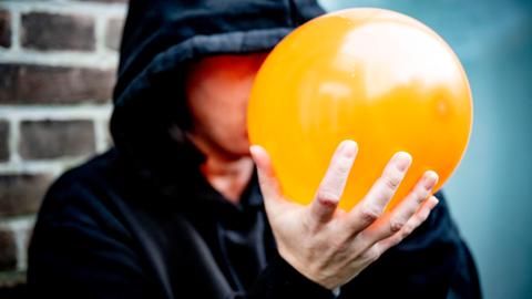 Ein Mann hält einen orangefarbenen Luftballon an seinen Mund