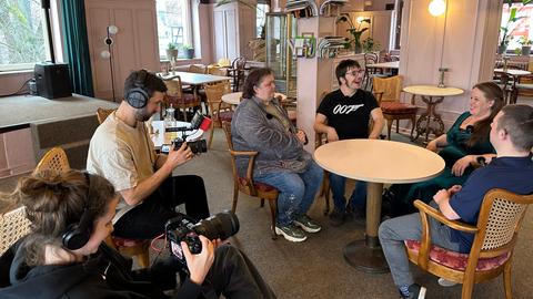 In einem Café in Marburg sitzen vier Menschen um einen Tisch herum. Davor hocken ein Kameramann und eine Kamerafrau und filmen die Gespräche.