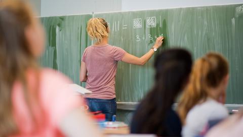 Eine Lehrerin schreibt Rechnungen an die Schultafel.