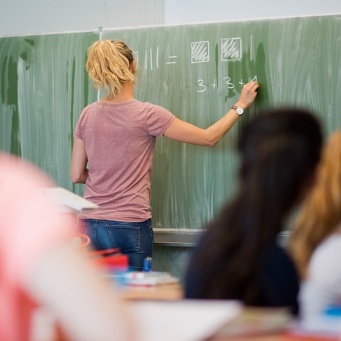 Eine Lehrerin schreibt Rechnungen an die Schultafel.