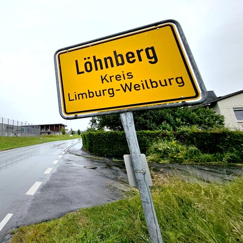 Ortsschild von Löhnberg im Vordergrund, im Hintergund eine Ortseinfahrt und einige Häuser