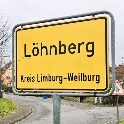 Ortsschild von Löhnberg im Vordergrund, im Hintergrund Straßen und einige Häuser